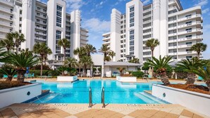A modern hotel with a central pool surrounded by palm trees and lounge chairs. - Harbor Landing 101b (Destin)