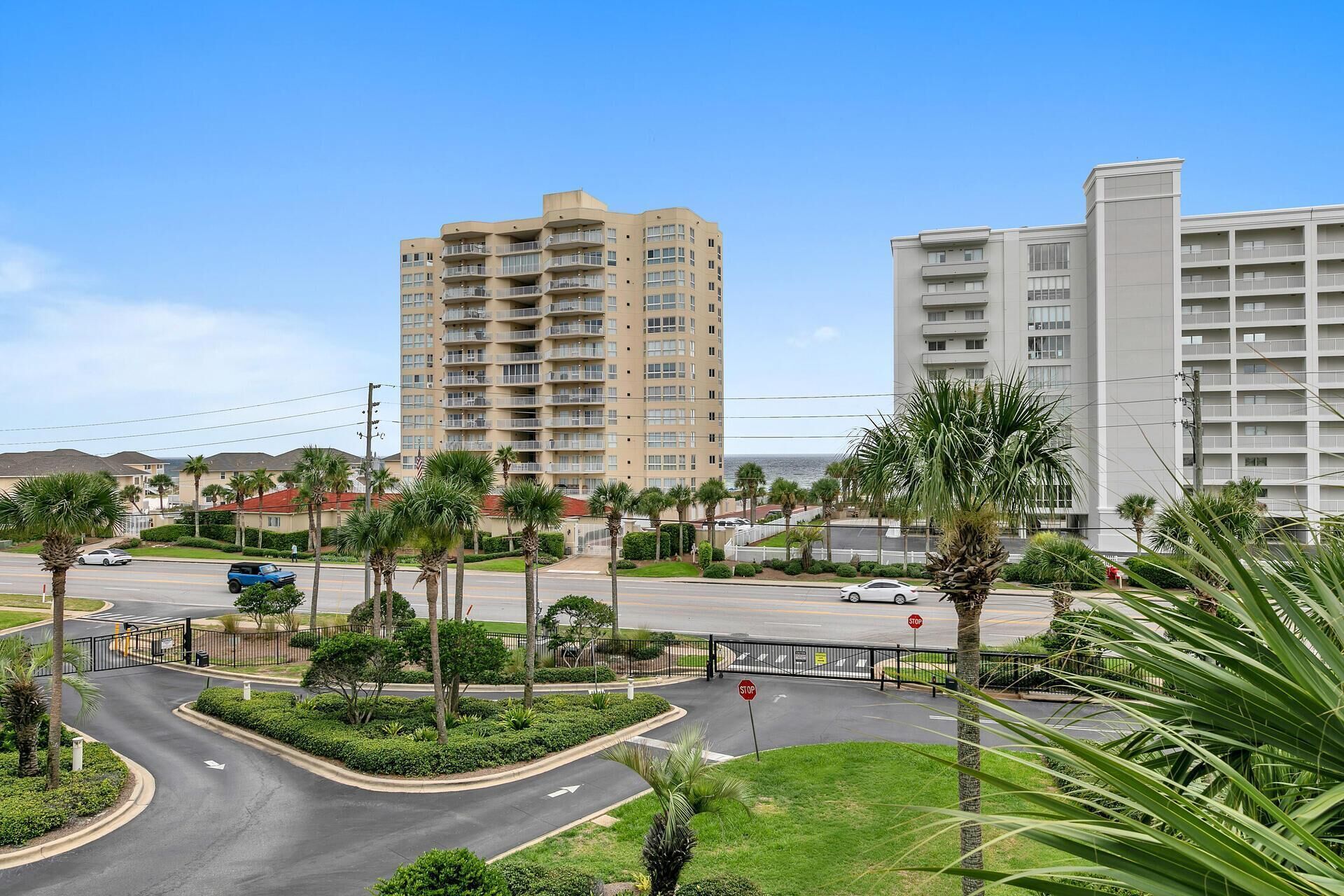 A multi-story hotel with balconies, a parking area, and palm trees.