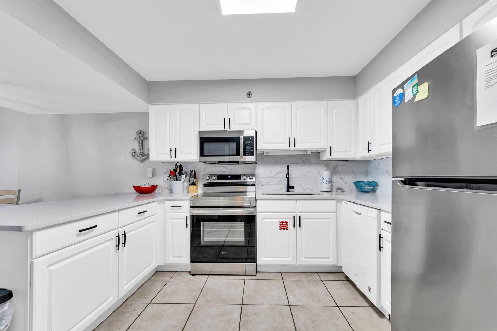Una cucina moderna con mobili bianchi, elettrodomestici in acciaio inossidabile e pavimento piastrellato.