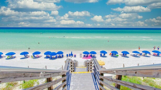 A beach with a wooden staircase leading down to the sand, rows of blue umbrellas, and clear turquoise water. - Beachcrest 101 (Santa Rosa Beach)