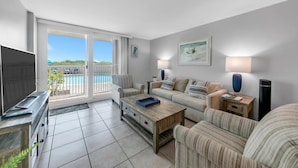 A spacious living room with a large TV, a sofa, a coffee table, and a view of a pool. - Beachcrest 101 (Santa Rosa Beach)
