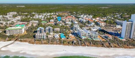 An aerial view of a coastal town with beachfront properties, dense residential areas, and a clear blue sky.