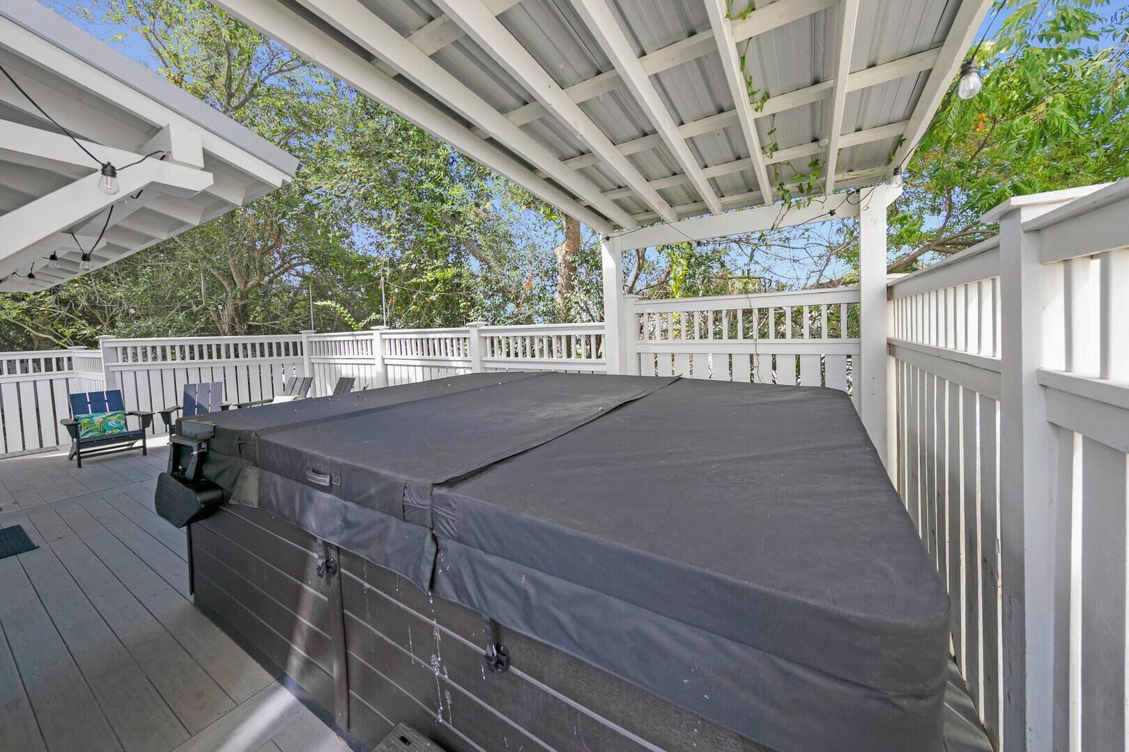 A covered hot tub area with a wooden deck, white railing, and outdoor furniture.