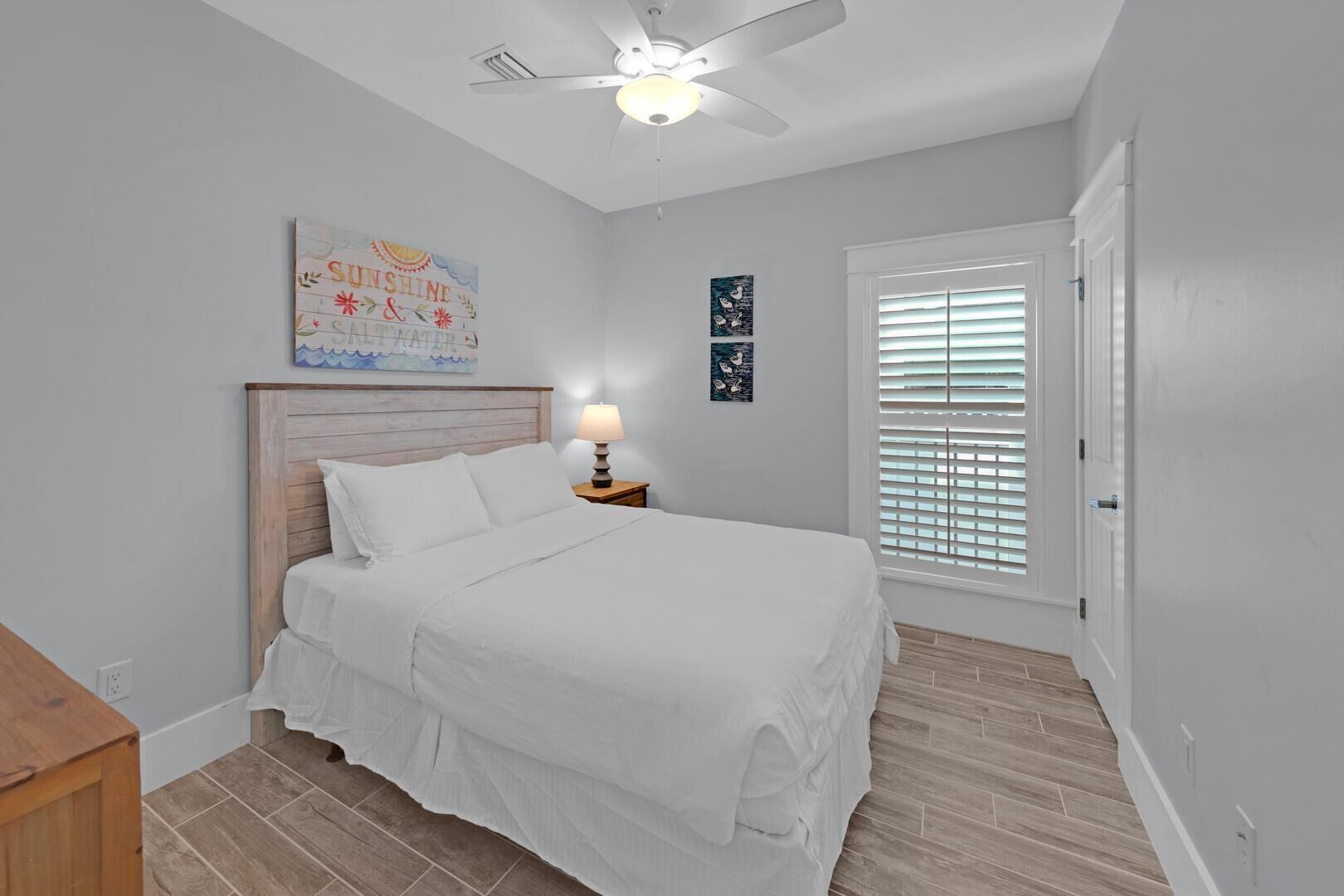A bedroom with a bed, a nightstand with a lamp, a ceiling fan, and a window with blinds.