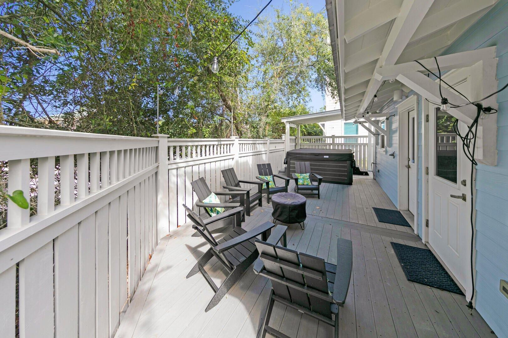 A covered outdoor deck with a white railing, multiple seating areas, and a hot tub.