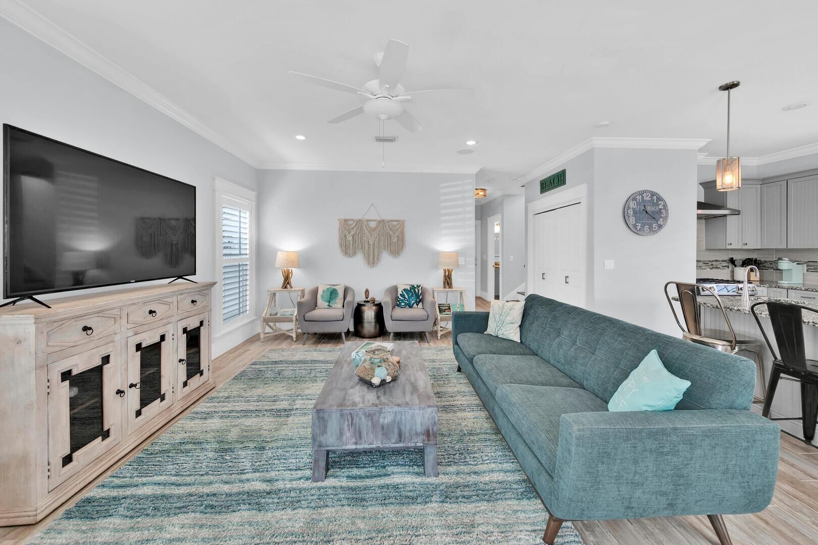 A modern living room with a flat-screen TV, two sofas, a coffee table, and a dining area with a kitchen in the background.