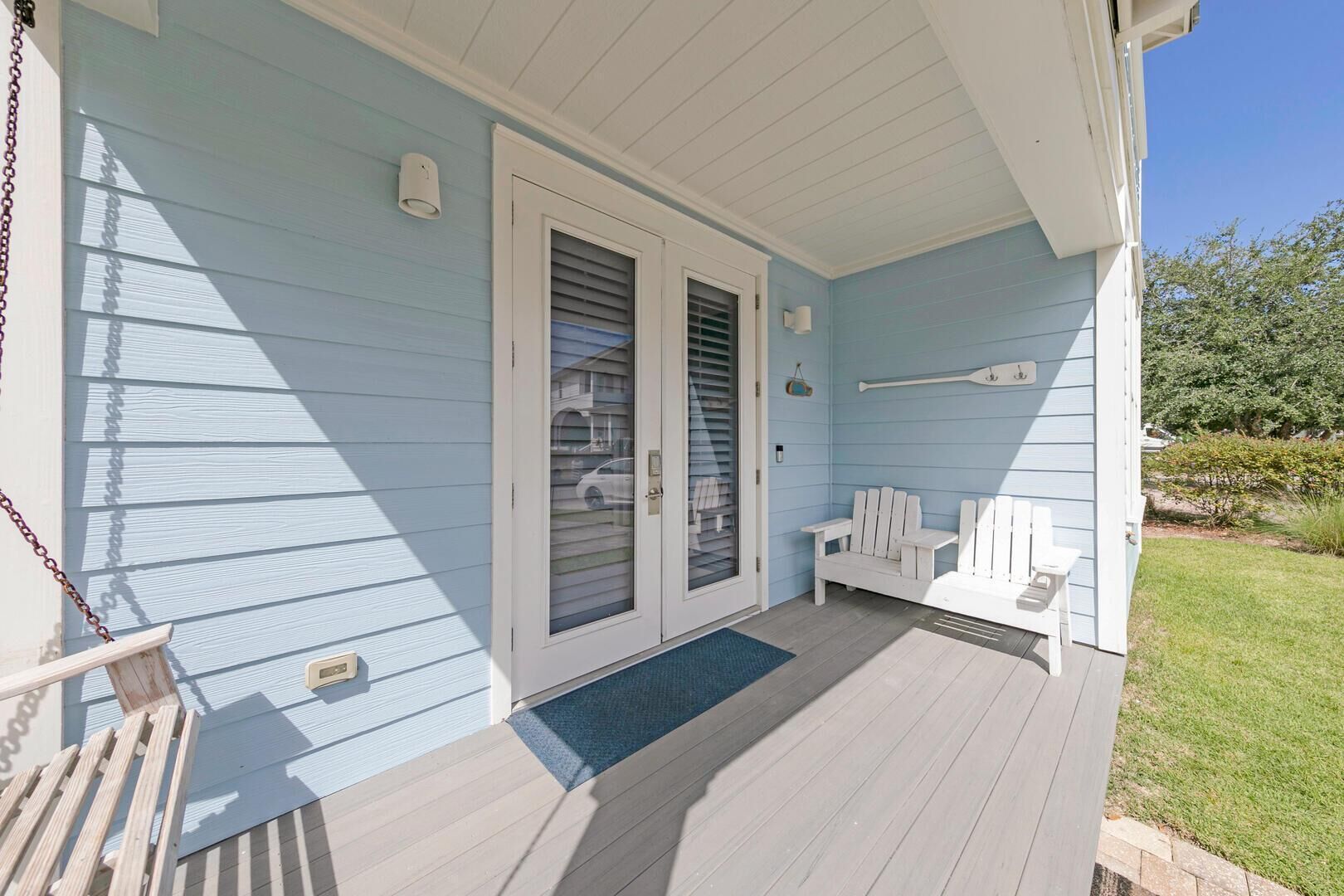 A covered porch with a wooden deck, a bench, and a door leading to a garage.