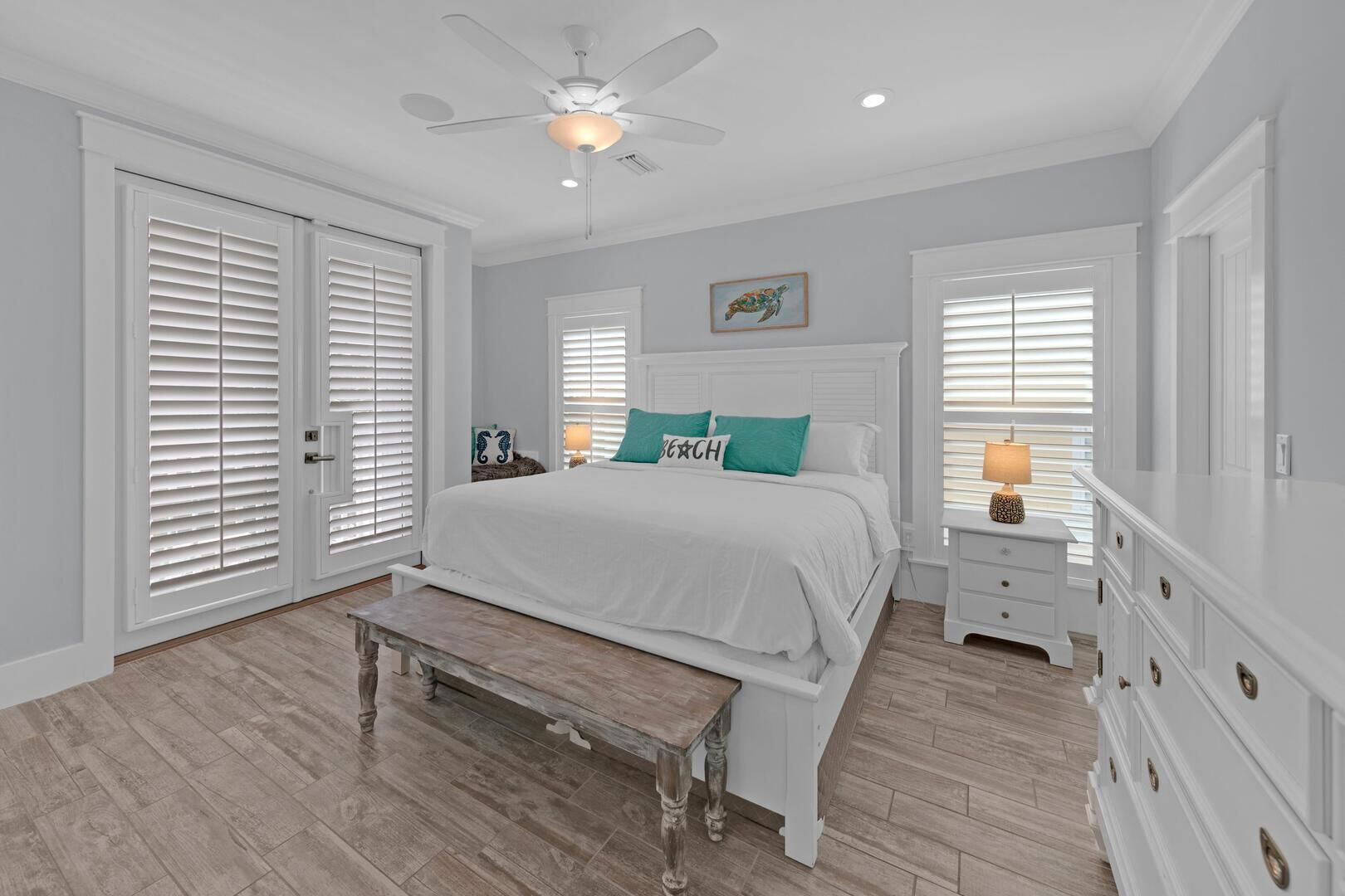 A bedroom with a bed, a bench, a nightstand, a dresser, a ceiling fan, and a window with blinds.