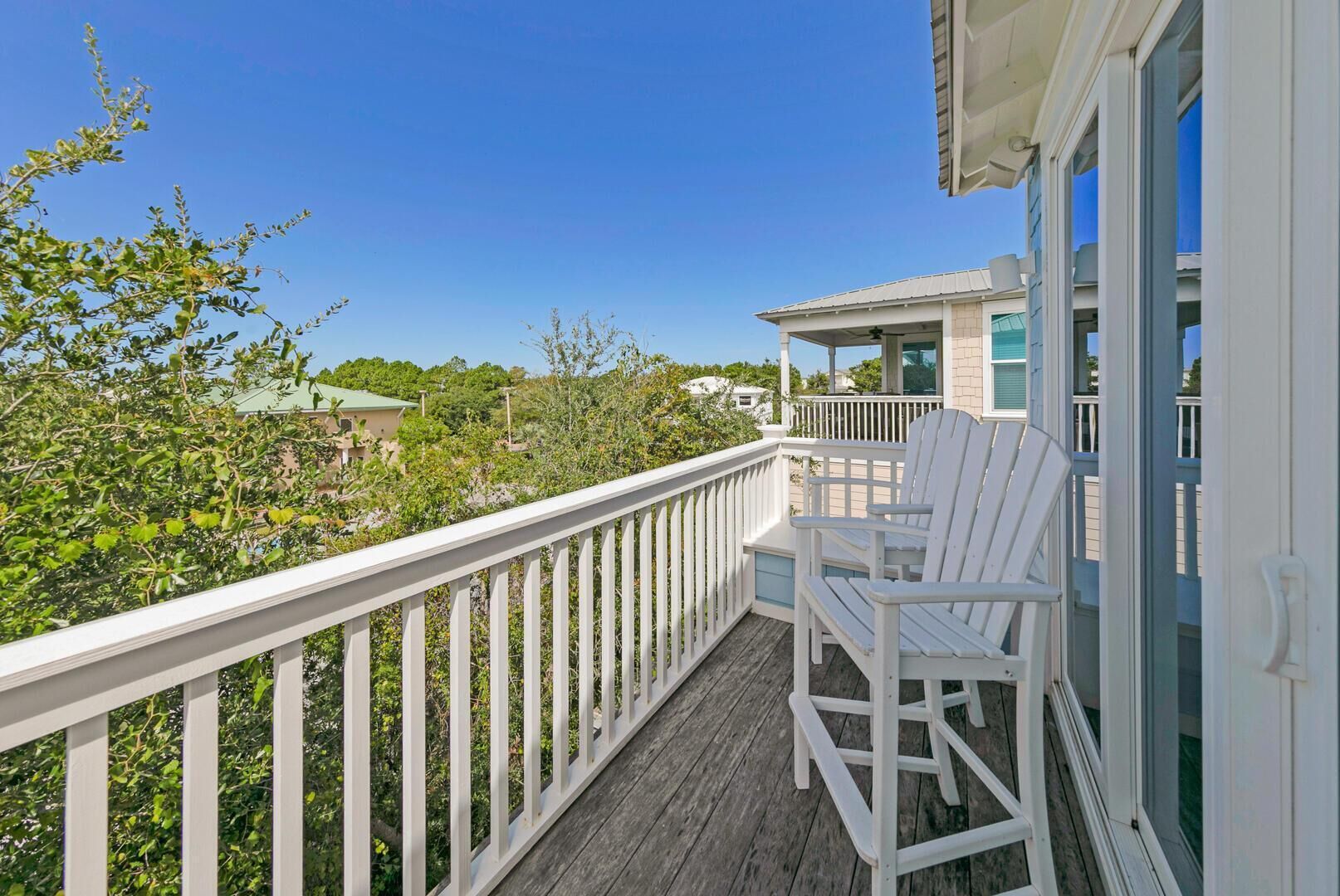 A wooden deck with white railings, two white Adirondack chairs, and a view of a house with a green roof and a covered porch.