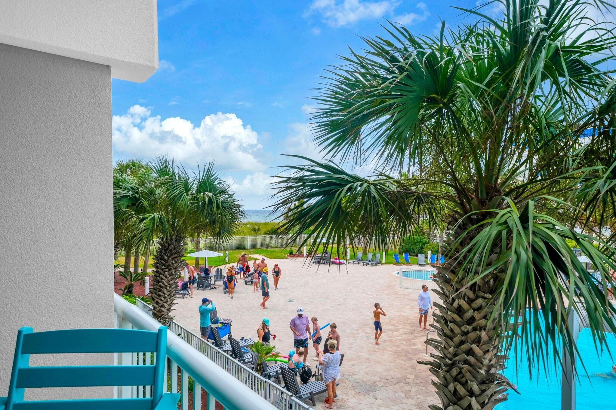 A poolside area with palm trees, lounge chairs, and people.