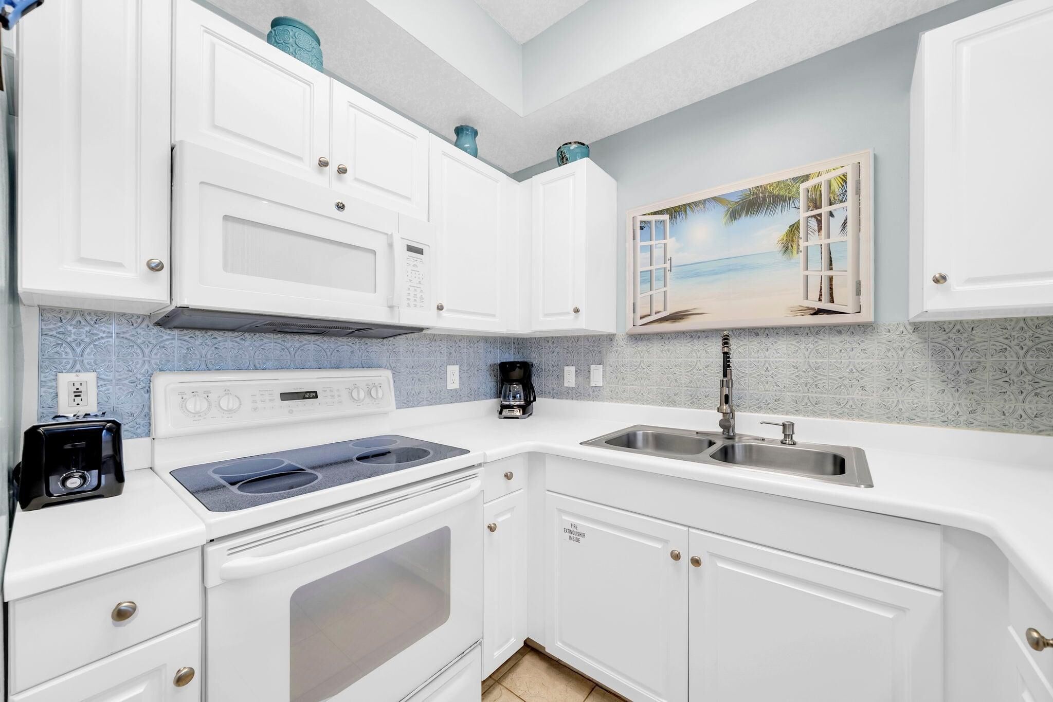 A compact kitchen with white cabinets, a stove, a microwave, a coffee maker, and a sink.