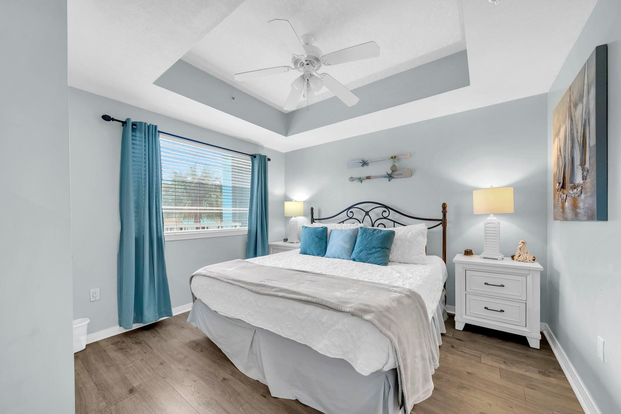 Une chambre à coucher avec un lit, une table de chevet, un ventilateur de plafond et une fenêtre avec des rideaux.