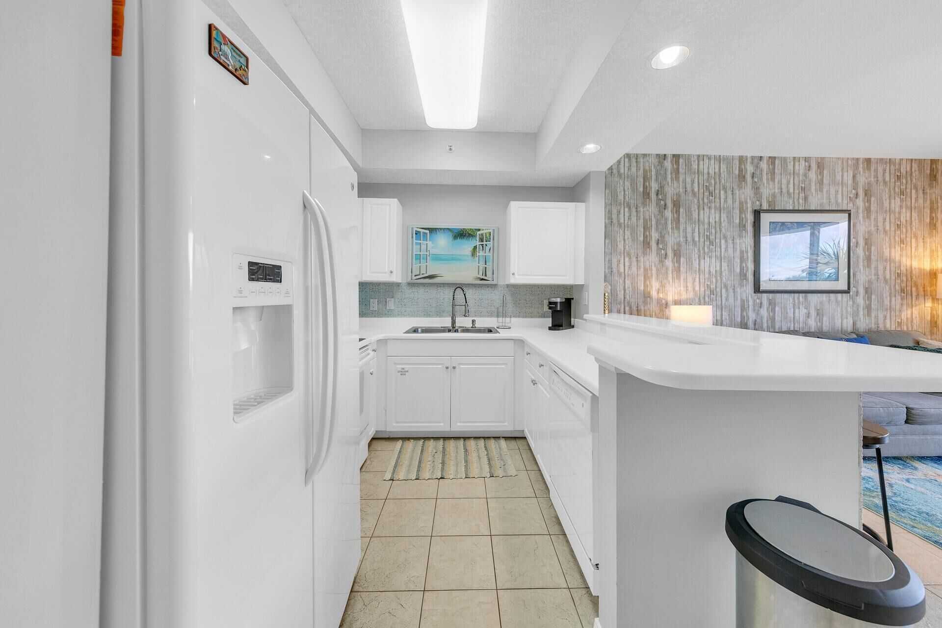 A modern kitchen with white cabinetry, a built-in water dispenser, a sink, and a small island with a coffee maker.