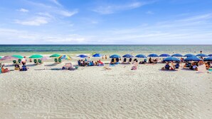 A beach with multiple umbrellas and beach chairs, some people sunbathing, and a clear blue sky.