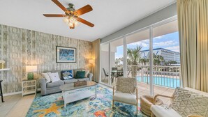 A spacious living room with a large window, a ceiling fan, and a colorful starfish-patterned rug.