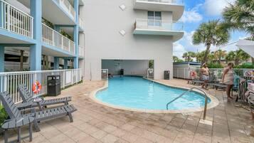 A swimming pool with lounge chairs and a lifebuoy, surrounded by a building with balconies.