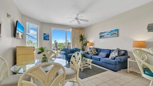 A living room with a blue sofa, white wicker chairs, a glass coffee table, and a ceiling fan. - Destin West Gulfside 304 (Fort Walton Beach)