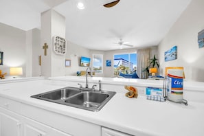 A modern kitchen with a double sink, white countertops, and a view of a building outside. - Destin West Gulfside 304 (Fort Walton Beach)