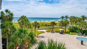 A pool area with lounge chairs and umbrellas, surrounded by palm trees and a view of the beach and ocean. - Destin West Gulfside 304 (Fort Walton Beach)