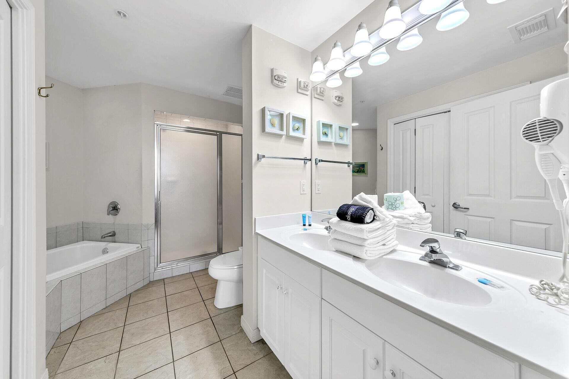 Een moderne badkamer met een grote spiegel, een douche, een bad en een wastafel met een haardroger.