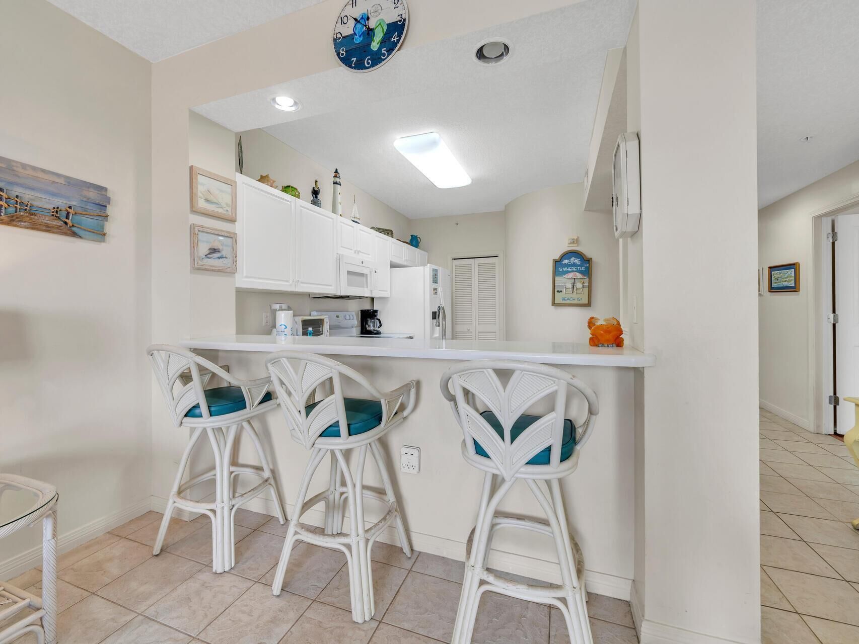 A kitchen with white cabinets, a white countertop, and three white bar stools with teal cushions.