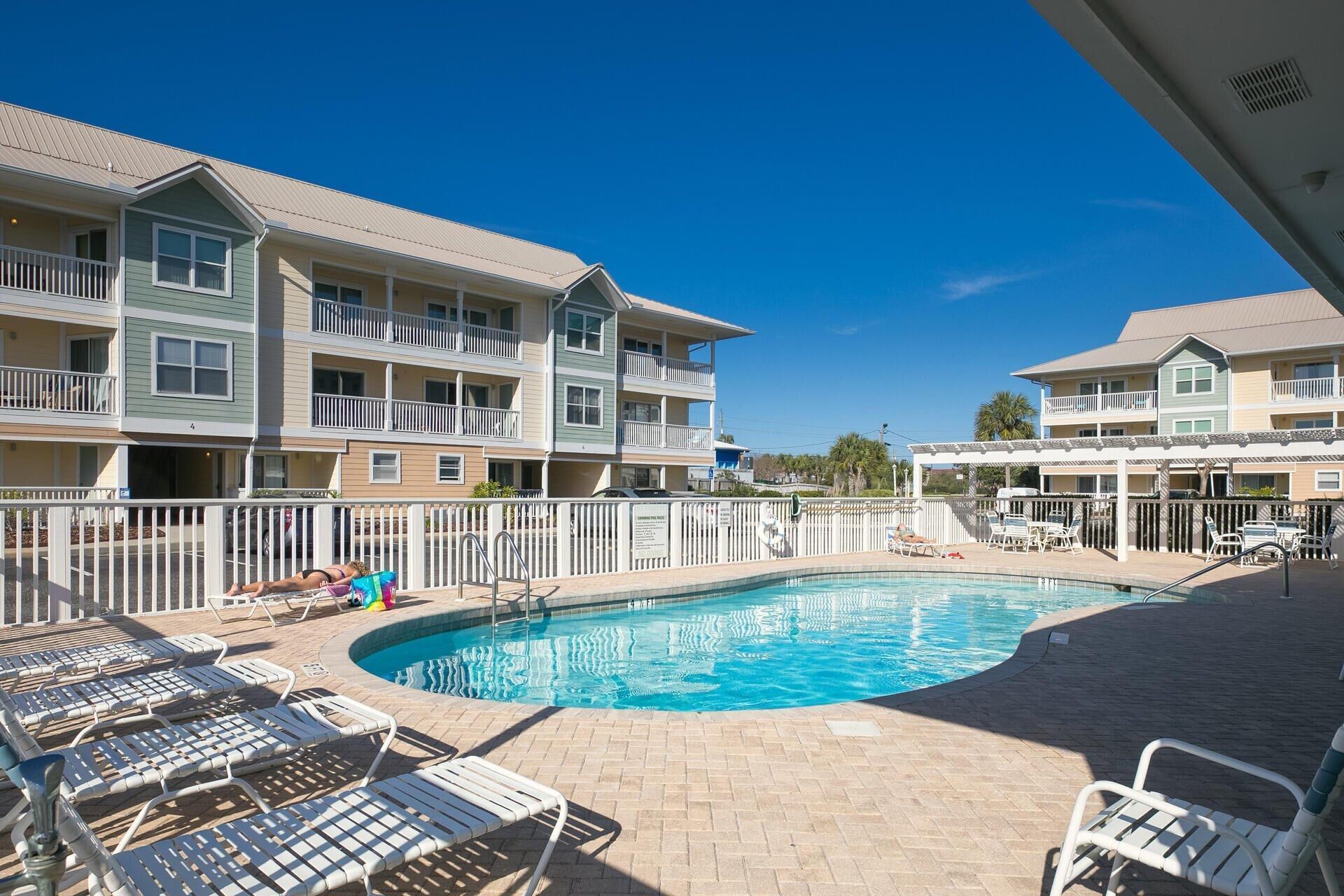 A pool area with lounge chairs, a fenced swimming pool, and multi-story buildings with balconies.