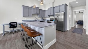 Una cocina moderna con gabinetes grises, un refrigerador de acero inoxidable y una isla de mármol con taburetes de bar.