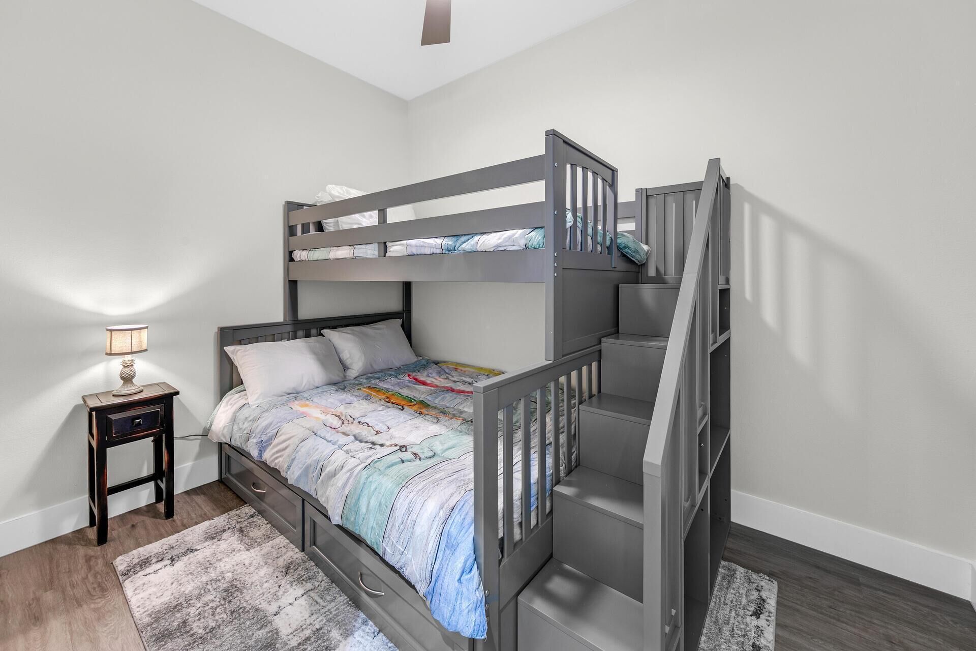 A bunk bed with a wooden frame, a nightstand with a lamp, and a patterned rug.