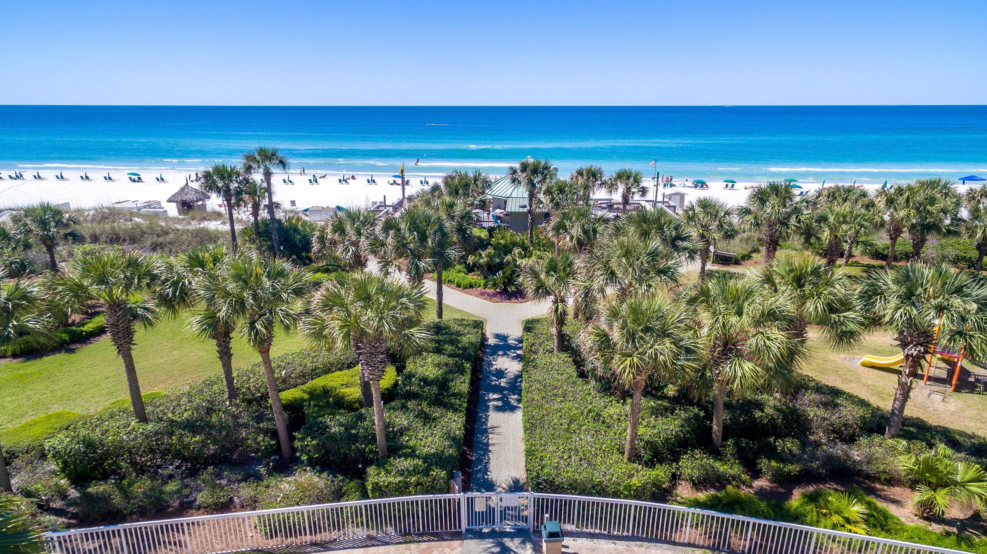A beach resort with a pathway leading to the beach, surrounded by palm trees and a view of the ocean.