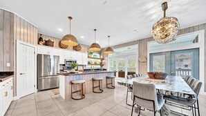 A modern kitchen with white cabinets, stainless steel appliances, and a central island with stools. - Cloud Nine (Santa Rosa Beach)