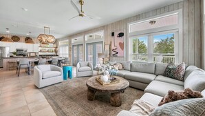 A spacious living room with a large sectional sofa, a coffee table, and a dining area with a kitchen in the background. - Cloud Nine (Santa Rosa Beach)