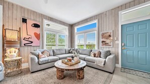 A modern living room with a grey sectional sofa, a round coffee table, and a large window with blinds. - Cloud Nine (Santa Rosa Beach)
