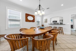 A dining area with a wooden table and chairs, a chandelier, and a kitchen in the background. - A Spyglass (Destin)