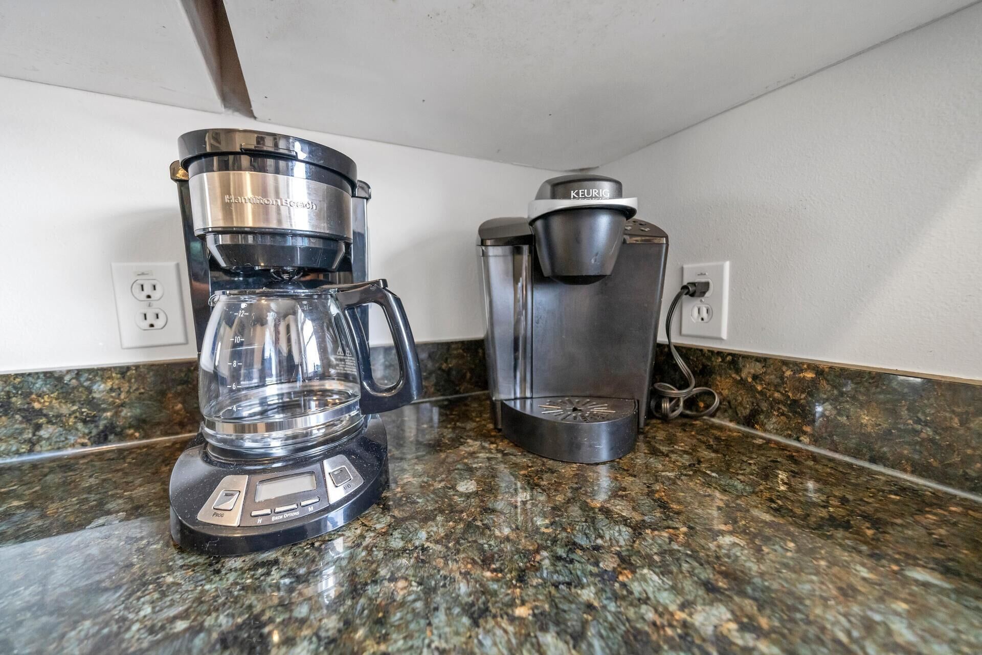 A coffee maker and a Keurig on a granite countertop.