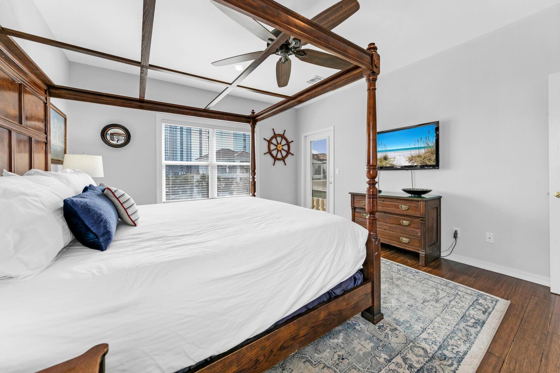 A four-poster bed with a ceiling fan, a television, a dresser, and a window with blinds.