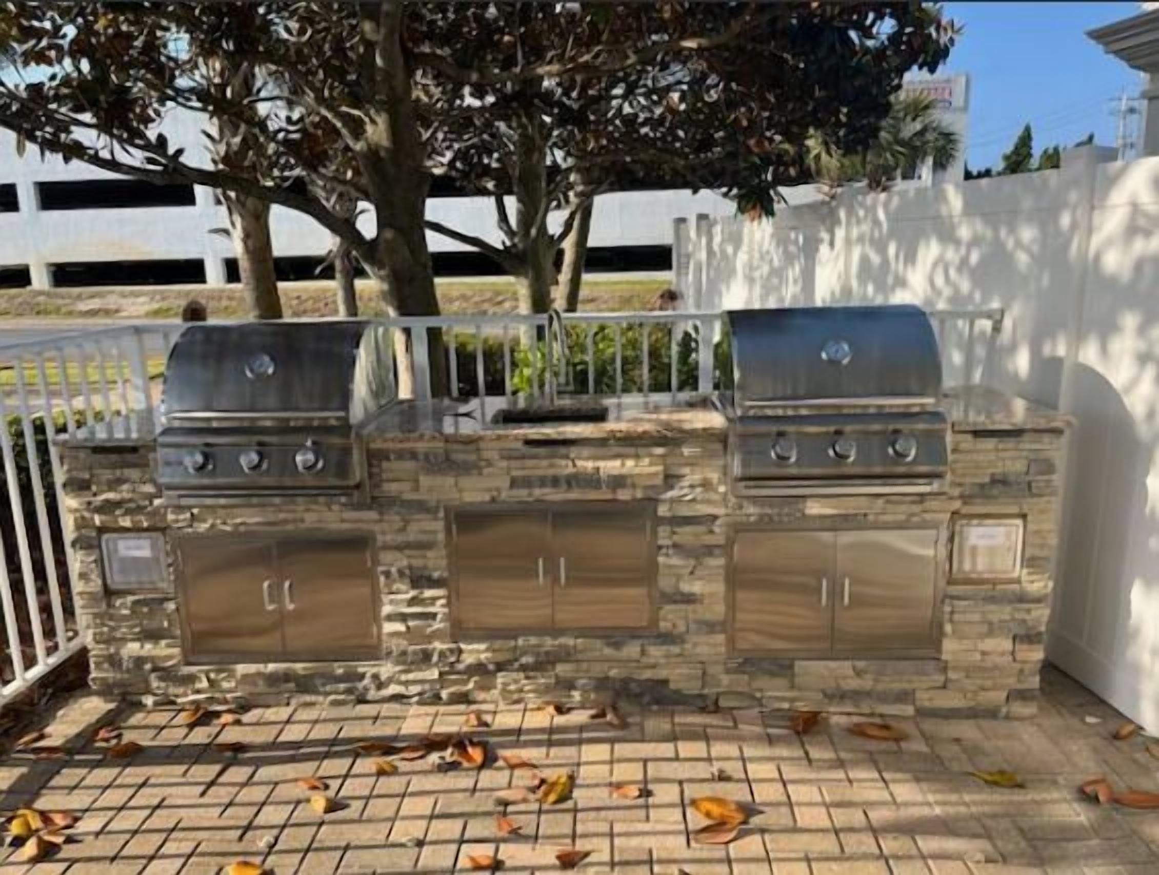 An outdoor barbecue grill with a stone facade and two side cabinets.