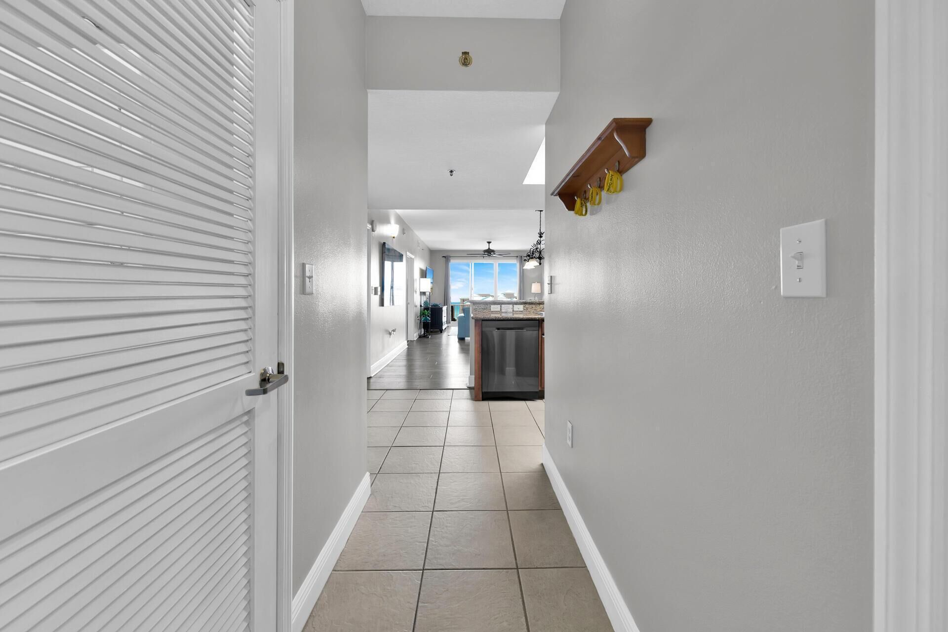 A hallway with a closed door, a kitchen area with a dishwasher, and a ceiling fan.