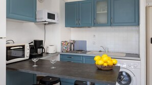 A compact kitchen with a microwave, toaster, coffee maker, and a washing machine. There are bar stools and a bowl of lemons on the counter. - Apartment Aloes by Interhome (Llançà)
