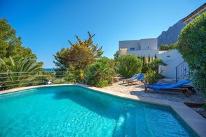 Une piscine d’un bleu éclatant, dotée de chaises longues et offrant une vue sur une montagne en arrière-plan.