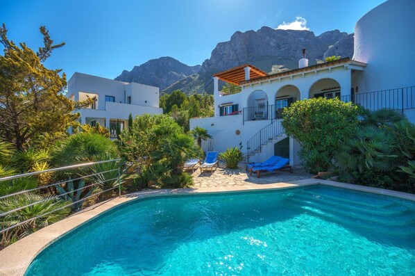 Une villa moderne dotée d’une piscine, entourée d’une végétation luxuriante et avec des montagnes en toile de fond.
