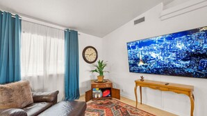 A living room with a leather sofa, a patterned rug, a wall clock, a television, and a cityscape painting. - Lake View • Hot Tub • RV/Boat Parking • Fire Pit (Lake Havasu City)