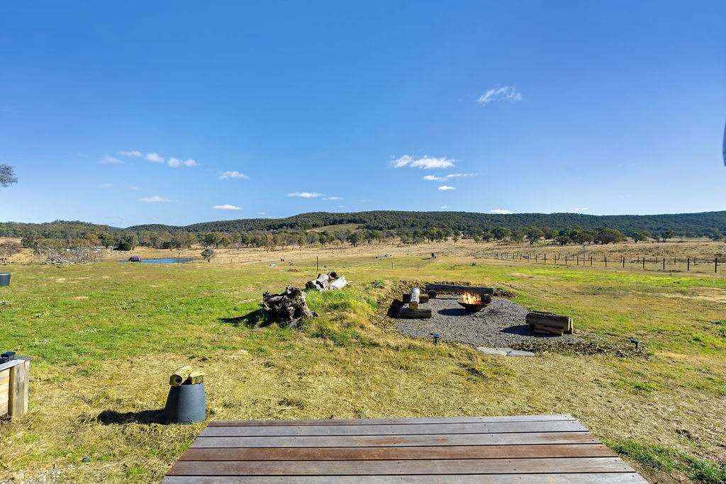 A wooden deck leading to a grassy field with a fire pit and a pond in the distance.