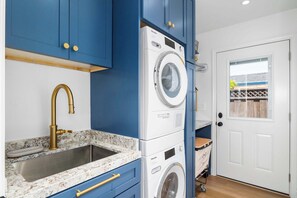 Ein kleiner Hauswirtschaftsraum mit Waschmaschine, Waschbecken mit goldfarbenem Wasserhahn und blauen Schränken.