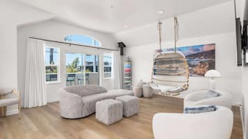 Uma sala de estar espaçosa com um amplo sofá de canto, uma cadeira suspensa e vista para o exterior através de grandes janelas.
