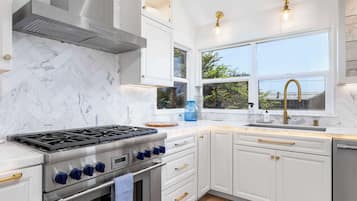 Uma cozinha moderna com armários brancos, fogão de aço inoxidável e uma janela com vista para o verde.