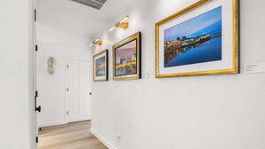Un pasillo con paredes blancas, piso de madera y tres obras de arte enmarcadas.