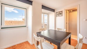 Un coin repas avec une table et des chaises, une fenêtre donnant sur les toits et une porte menant à un balcon.