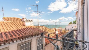 On aperçoit des toits recouverts de tuiles en terre cuite, la mer au loin et un ciel dégagé.