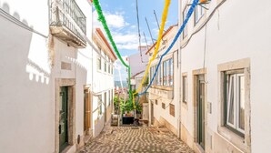 Une rue étroite pavée de pierres, bordée de bâtiments blancs dotés de balcons, et agrémentée de décorations colorées suspendues au-dessus.