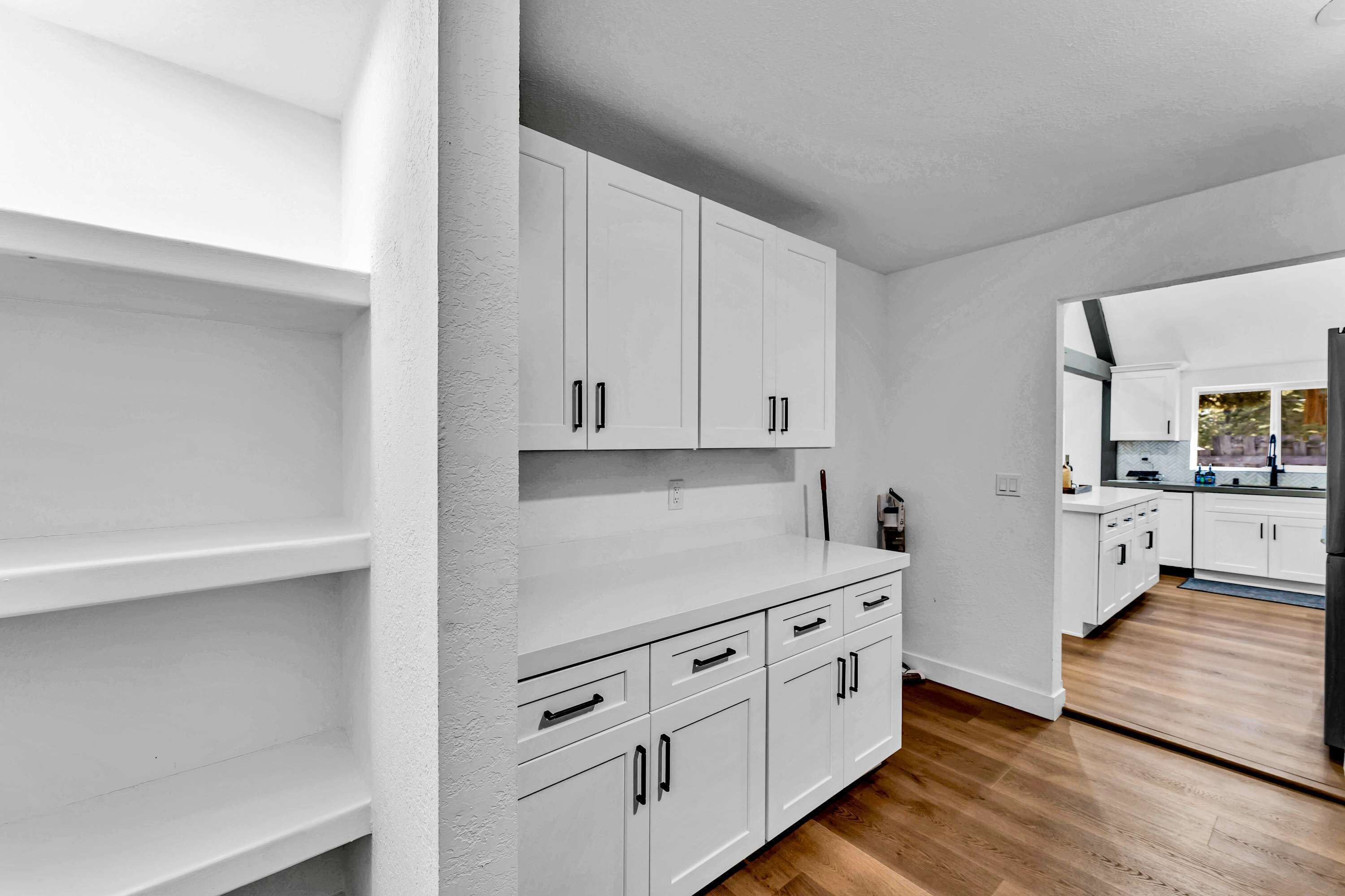 Una cocina moderna con armarios blancos, suelo de madera y vistas al comedor.
